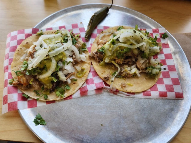 Two tacos on checkered butcher paper with a jalepeno pepper as garnish 